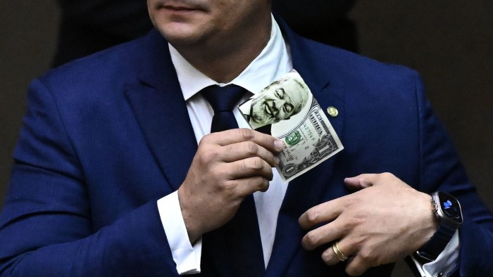 A politician holds  holds a US $1 bill with an image of Brazil’s President Luiz Inacio Lula da Silva on it in Brazil’s Congress this week