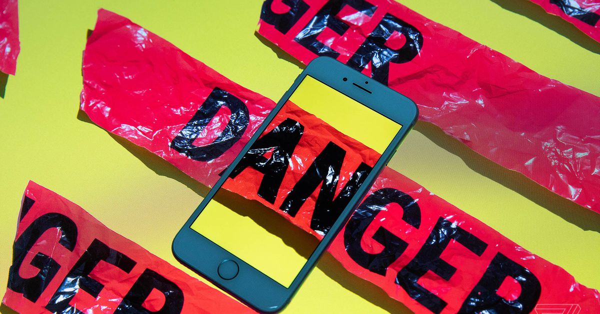 A smartphone sits on top of a surface with red tape reading “DANGER.” Where one strip intersects the phone, it continues inside the phone’s screen.