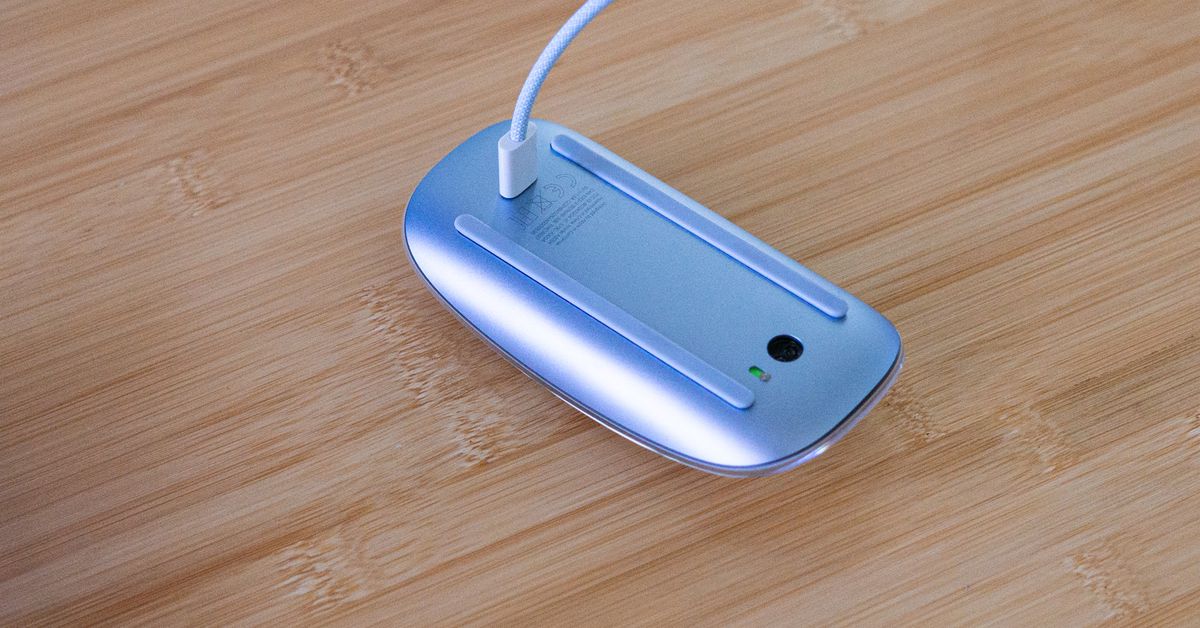 Picture of a Magic Mouse with USB-C laying upside-down with a charging cable plugged into it.