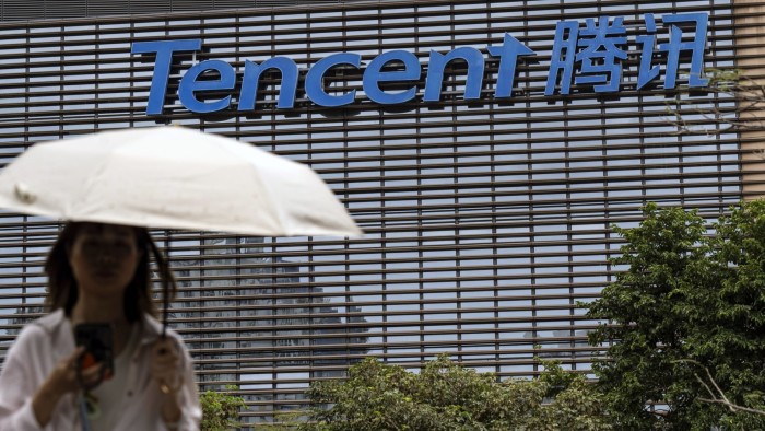 A person carrying an umbrella walks past the Tencent building