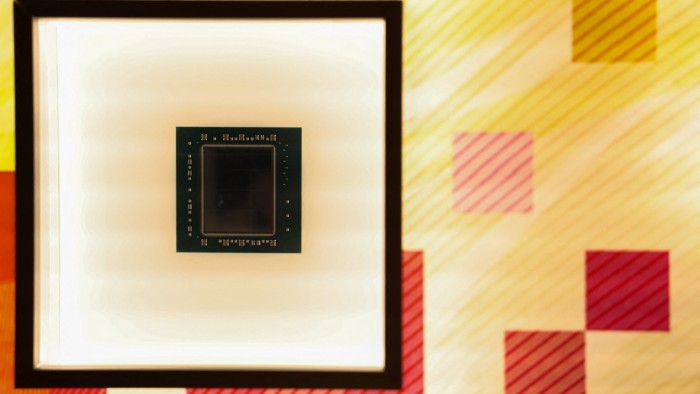 A semiconductor chip is displayed in a framed exhibit at the Taiwan Semiconductor Manufacturing Company Museum of Innovation in Hsinchu. The background features a colorful, geometric pattern with diagonal lines and squares in red and yellow hues.