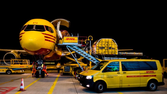 DHL Express employees unload cargo from a yellow DHL aircraft at the company's hub in Leipzig, Germany