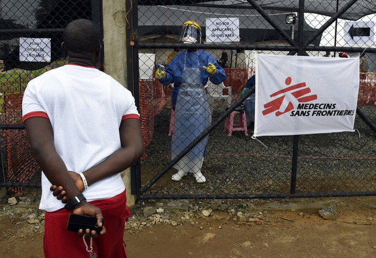 رجل يتحدث مع عامل صحي يرتدي ملابس واقية خلف السياج الأمني ​​في المركز الطبي لمنظمة أطباء بلا حدود.