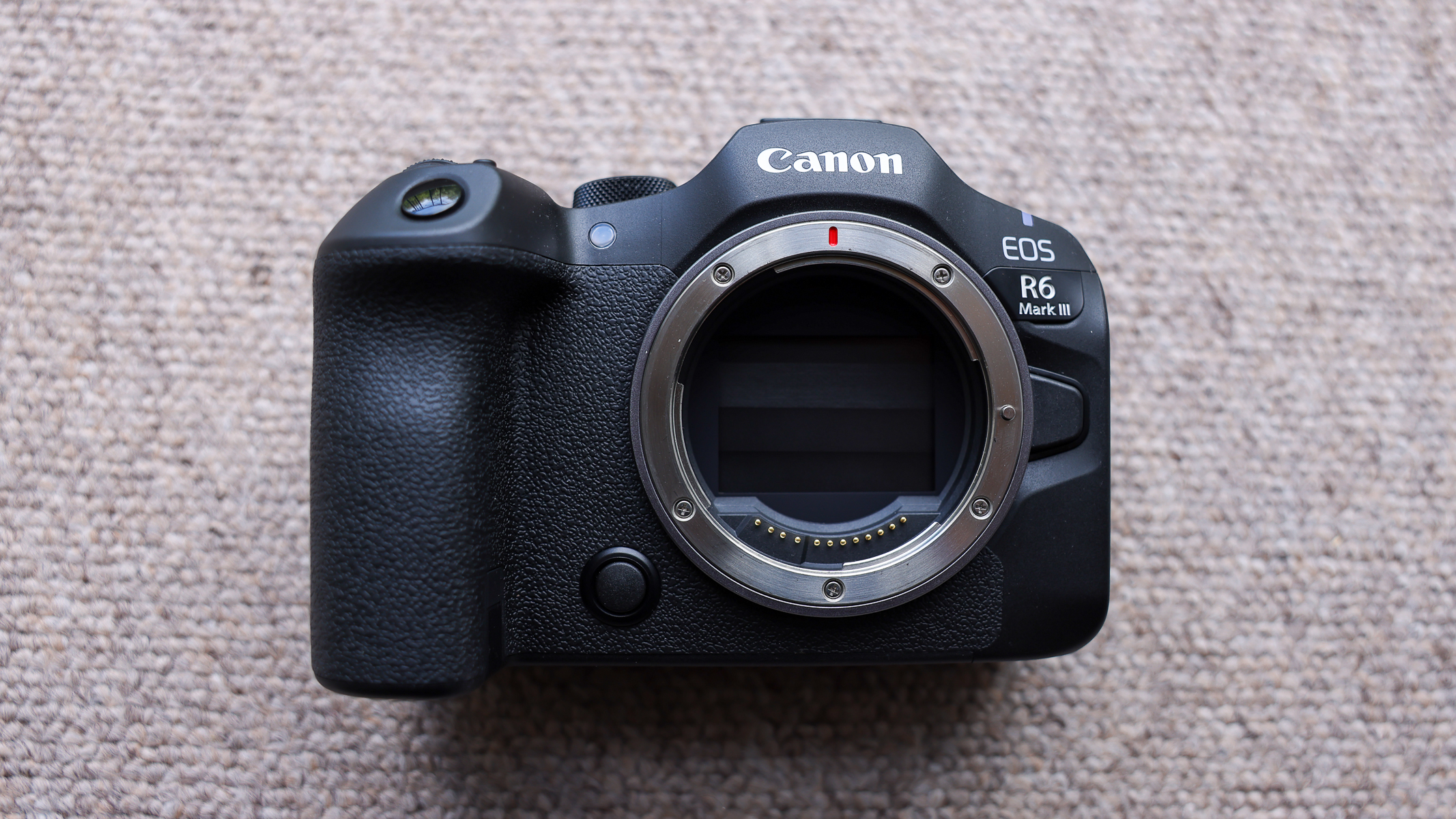 The front of the Canon EOS R6 III without a lens on a brown carpet.