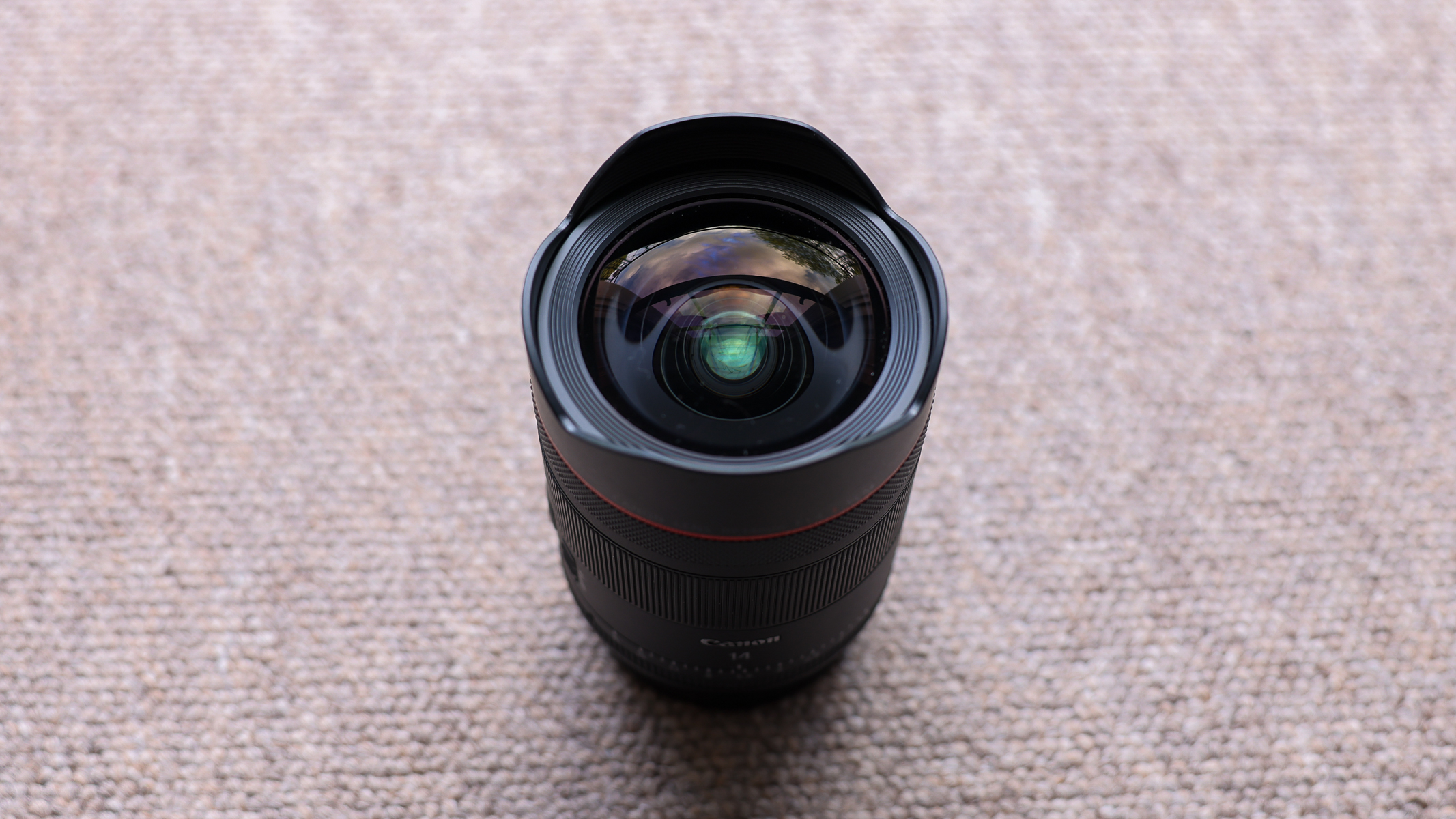 The Canon RF 14mm f/1.4 lens stood up on a brown carpet.