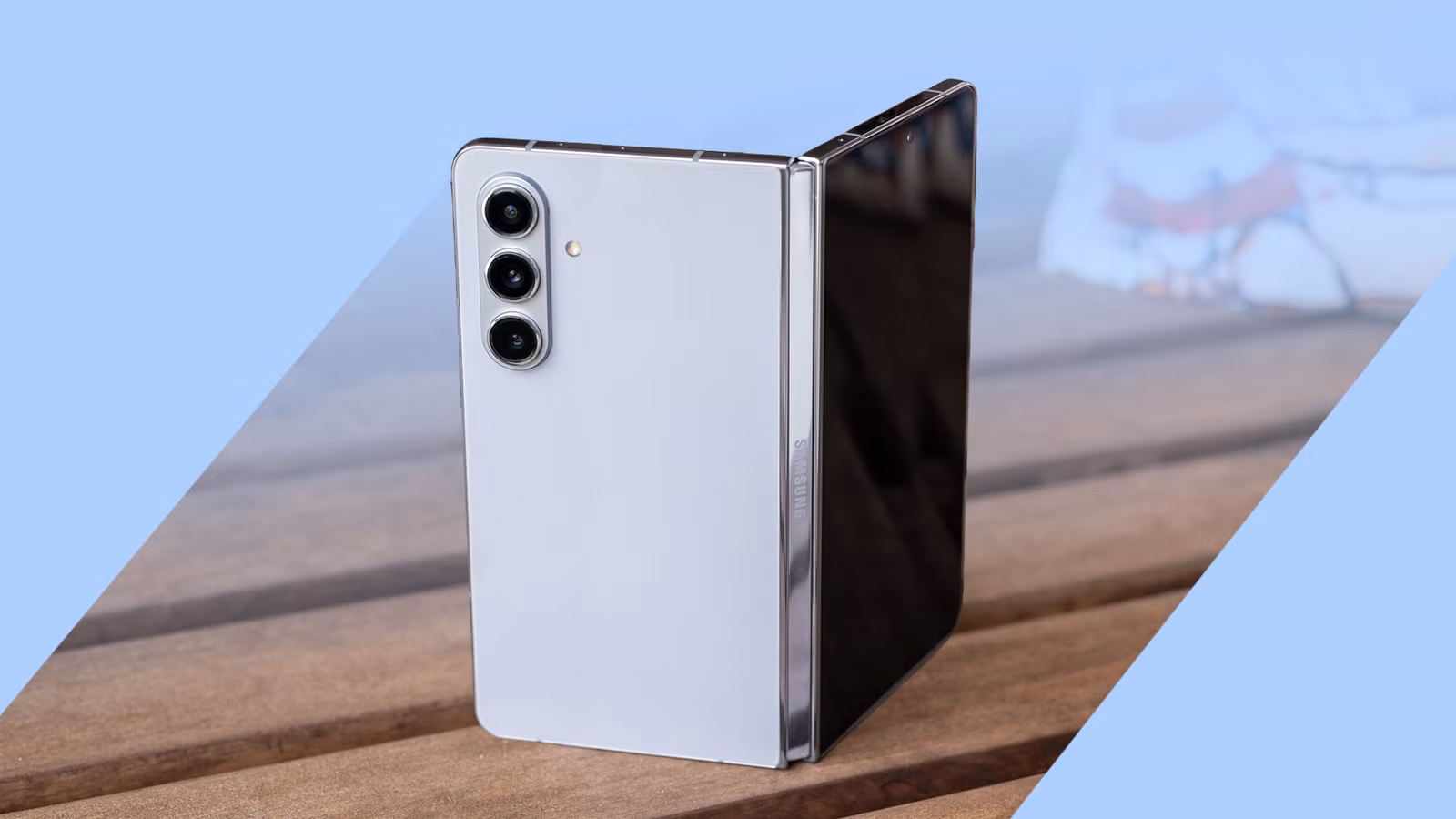 a silver samsung galaxy z fold phone stands partially open on a wooden table png